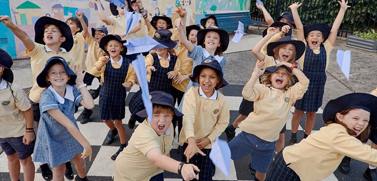 Primary_school_students-770x370 Students in school uniform, throwing paper planes in a school playground and smiling.