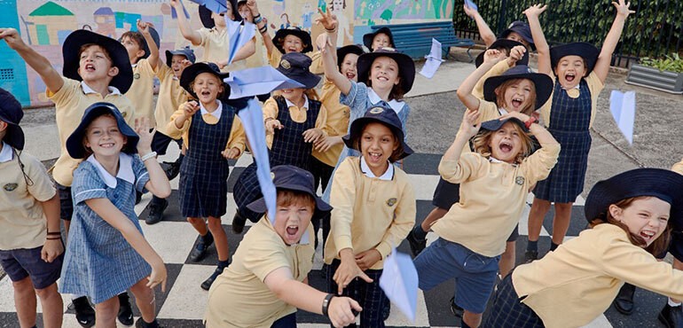 Students in school uniform, throwing paper planes in a school playground and smiling.